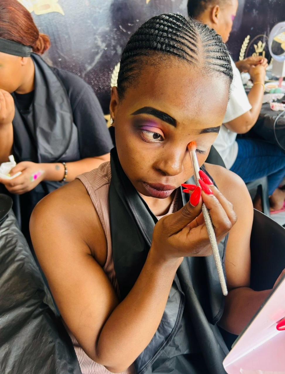 Student applying purple smokey eye shadow in class